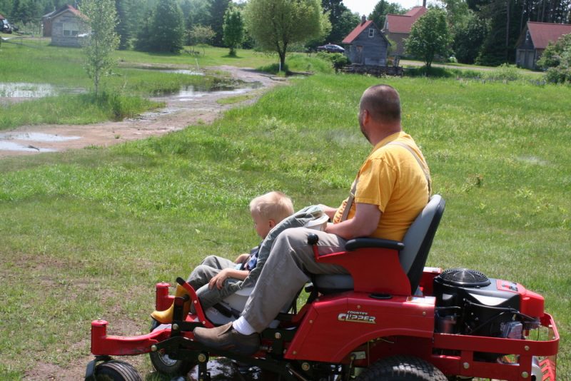 life on our own | ALS News Today | A photo from a few years ago shows Todd riding on a large, red lawn mower in rural Michigan, with a young Isaac strapped to a car seat on the mower's front deck