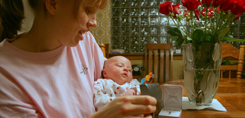 finding patterns | ALS News Today | Kristin holds her newborn daughter, Sara, while looking at jewelry boxes next to a vase of red roses.