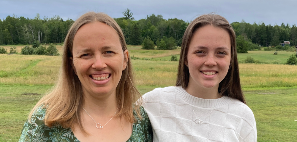 finding patterns | ALS News Today | Kristin and her daughter, Sara, wear matching silver necklaces and smile while posing in front of a field with their arms around each other.