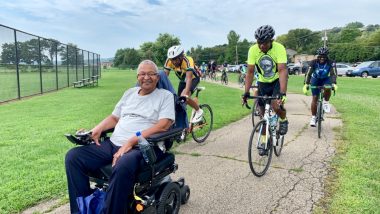 pace lining | ALS News Today | James Clingman rides down an outdoor path on his motorized wheelchair, as a number of bike riders follow behind him in a pace line.