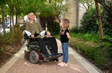 Researcher Avi Kremer sits in a power wheelchair and looks at his daughter, Ella.