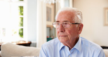 Older man sitting on a couch with a sad look on his face
