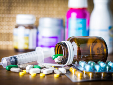 A variety of pills and medicines in bottles, plus a syringe