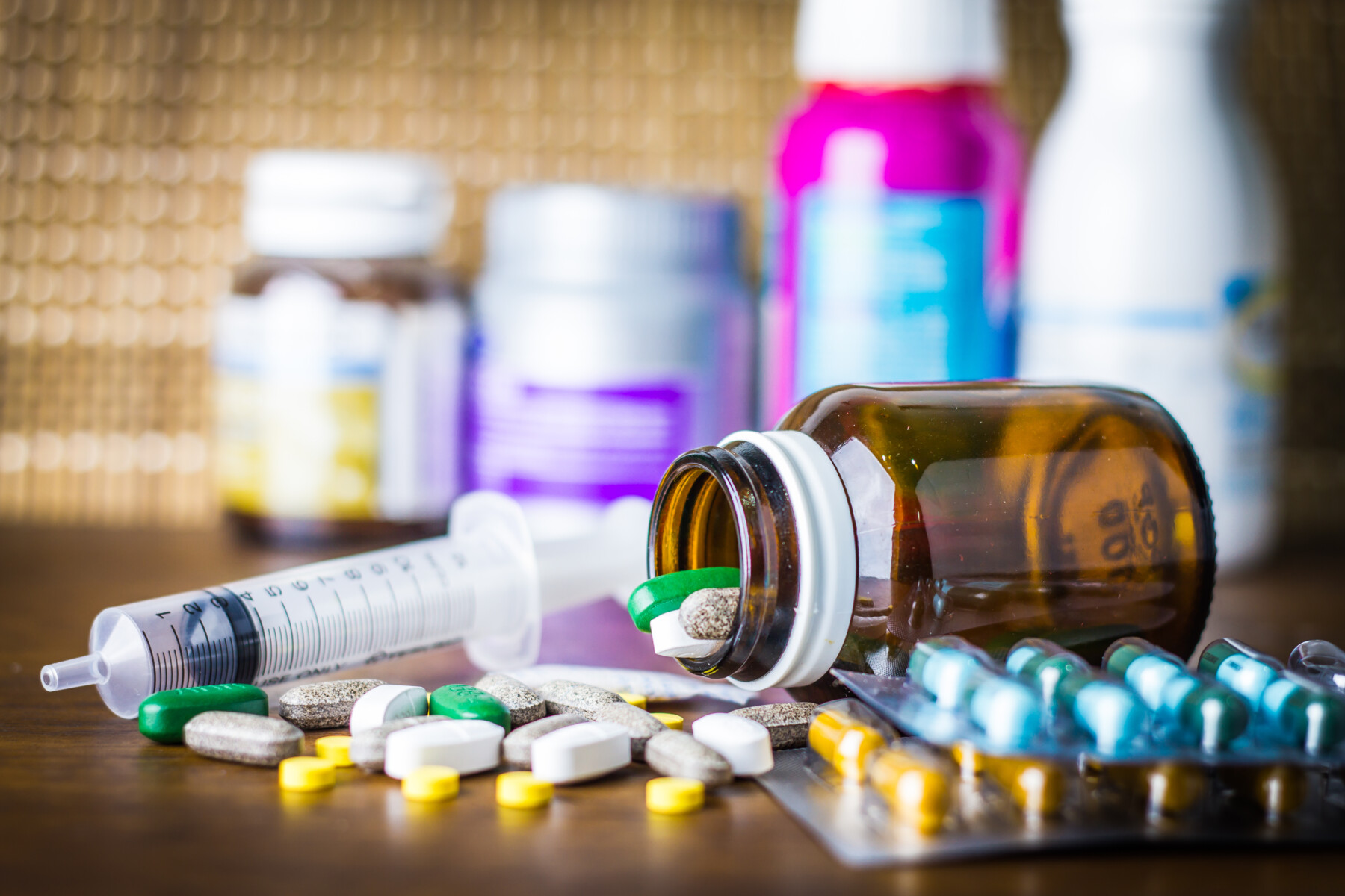 A variety of pills and medicines in bottles, plus a syringe