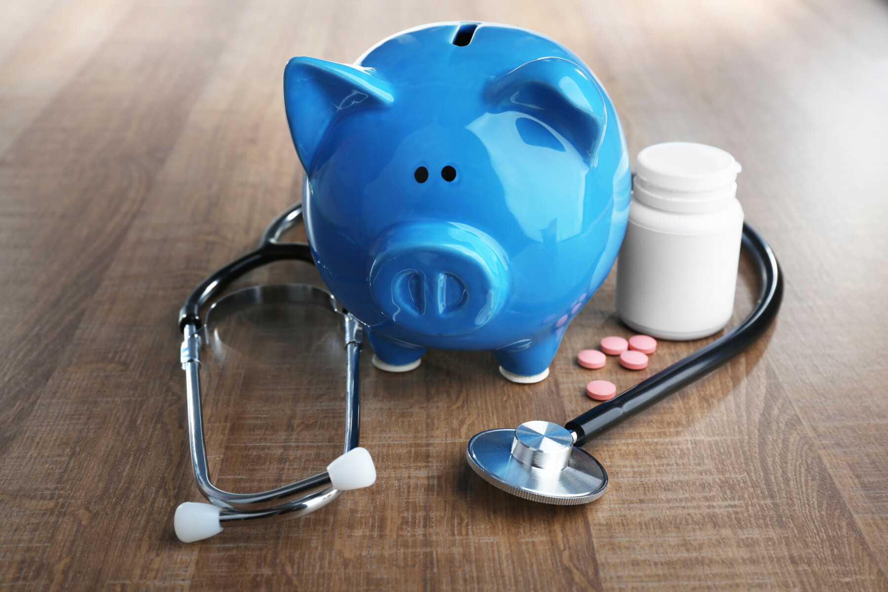 blue piggy bank with stethoscope and pill bottle