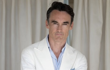 A headshot of a man with dark hair wearing a white medical coat.