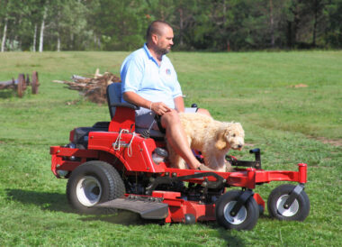 A man and a dog are shown atop a lawn mower.